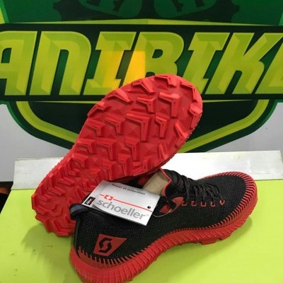 Sapatilhas de corrida pretas com sola vermelha em fundo verde