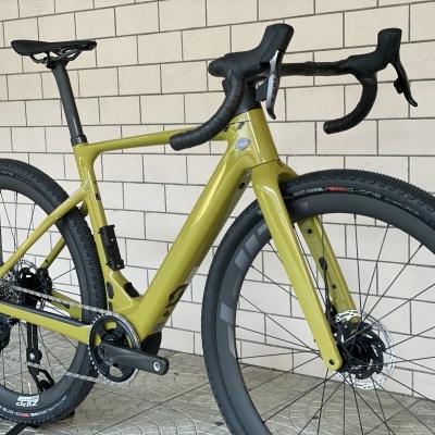 Bicicleta de estrada com quadro amarelo esverdeado e pneus pretos largos junto a parede clara de tijolos