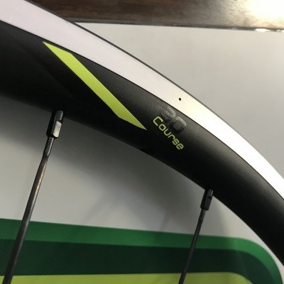 Roda de bicicleta com aro prateado e texto Course em verde