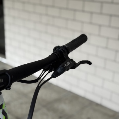 Punho de guiador de bicicleta preto com manete de travão com inscrição DB4 e parede de tijolo branca ao fundo.