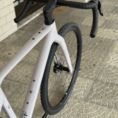 Bicicleta branca com guiador drop e pneus pretos em pavimento azulejado cinzento