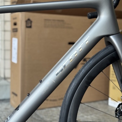 Parte de bicicleta cinzenta SCOTT com pneu preto na rua com caixas de cartão