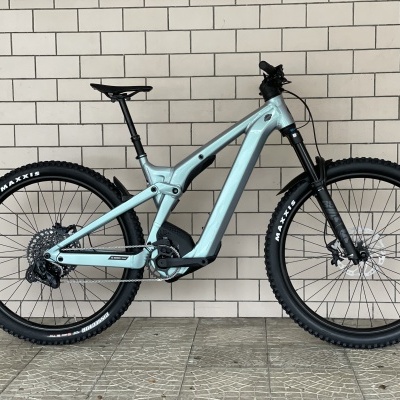 Bicicleta de montanha elétrica cinzenta clara encostada a uma parede de tijolos brancos