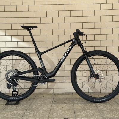 Bicicleta de montanha preta com texto SCOTT encostada a parede de tijolos