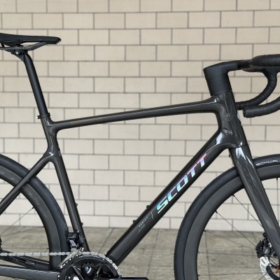 Bicicleta de estrada preta com texto SCOTT no quadro encostada a parede de tijolos