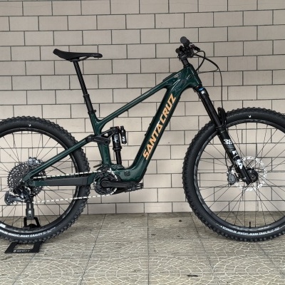 Bicicleta de montanha elétrica verde escuro parada contra muro de azulejos