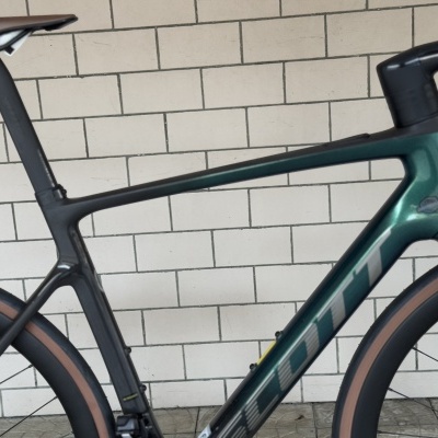 Bicicleta de estrada cinza e verde com pneus castanhos junto à parede de tijolos brancos