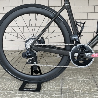 Roda traseira de bicicleta preta com componentes de mudança e pedaleira em suporte no chão cinzento