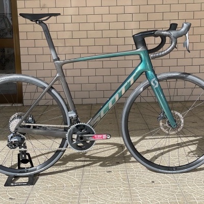 Bicicleta de estrada cinza e verde metálico encostada numa parede de tijolos claros