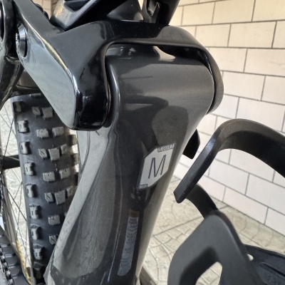 Quadro e suspensão de bicicleta preta com etiqueta tamanho médio e pneu grosso.