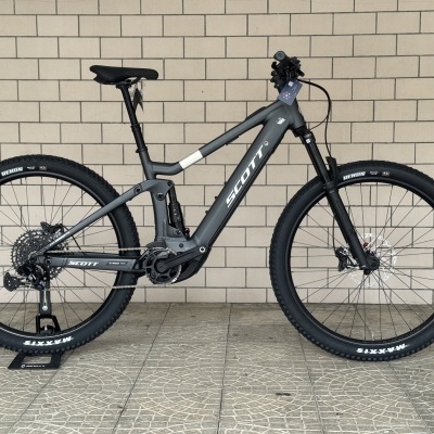 Bicicleta elétrica de montanha cinzenta escura com suspensão e pneus Maxxis Rekon