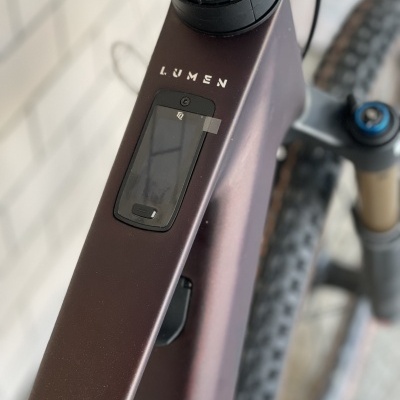 Bicicleta castanha com texto LUMEN no quadro e peça preta incorporada perto do guiador