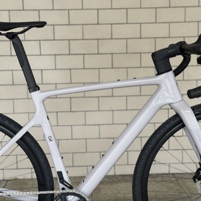 Bicicleta de estrada branca com guiador e selim pretos junto a parede de azulejos