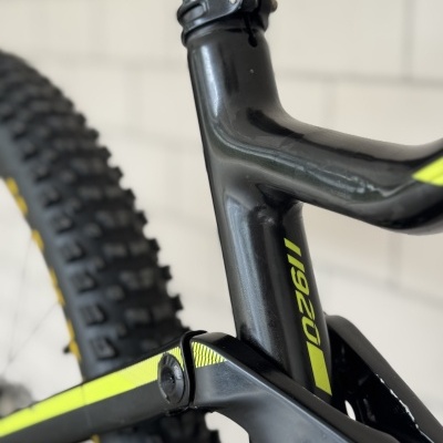 Detalhe do quadro preto e amarelo de uma bicicleta de montanha com pneu grosso ao fundo.
