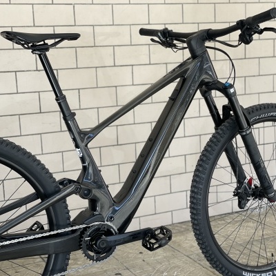 Bicicleta de montanha preta e cinzenta com pneus grossos perante uma parede de tijolos brancos