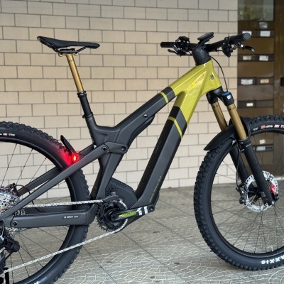 Bicicleta eléctrica de montanha verde e preta encostada numa parede de tijolos clara