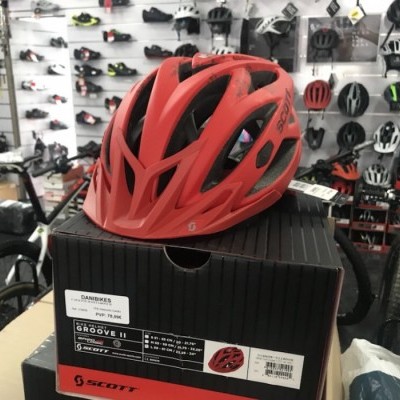 Capacete de bicicleta vermelho SCOTT sobre caixa preta em loja com outros capacetes ao fundo