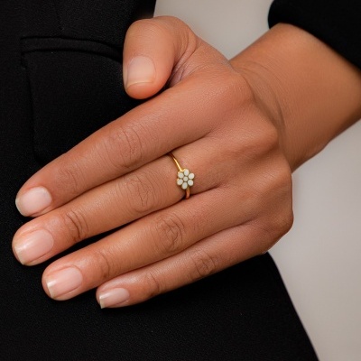 Anel dourado em forma de flor numa mão feminina sobre roupa preta