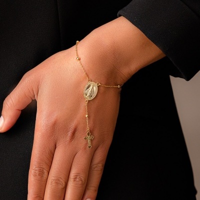 Pulseira em ouro com medalha oval e cruz pendente no pulso de mão direita