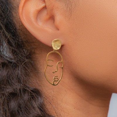 Brinco dourado pendente com design artístico de rosto estilizado
