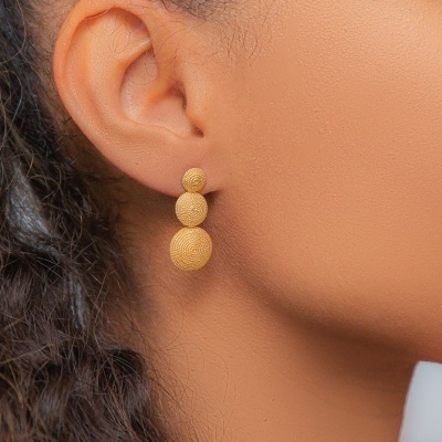 Brinco dourado de três esferas texturadas na orelha de uma mulher