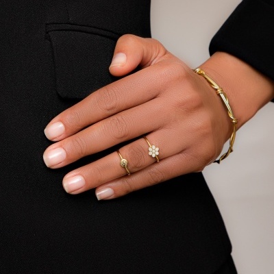 Mão feminina com anéis dourados e pulseira, vestida com fato preto