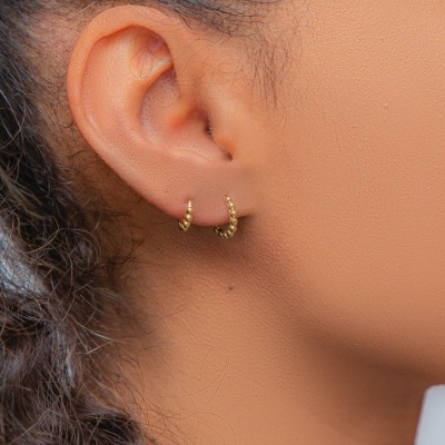 Brincos pequenos de ouro amarelo na orelha de uma pessoa