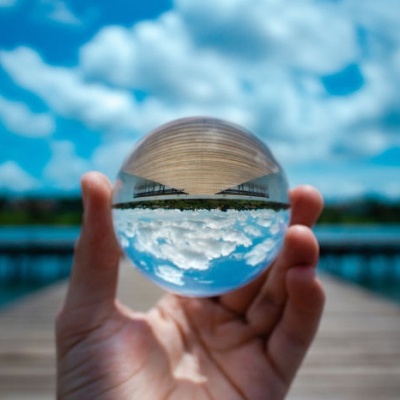 Mão segurando uma esfera de cristal com reflexo de céu, água e cais de madeira