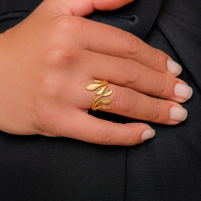Anel dourado com design de folhas numa mão contra fundo preto.