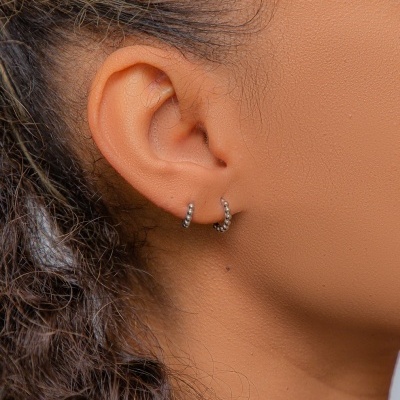 Brincos prateados em forma de argola com pedras brilhantes na orelha.