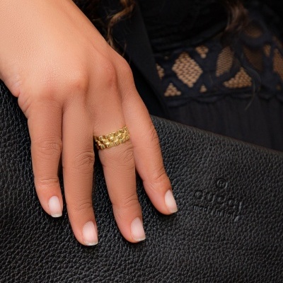 Mão feminina com anel dourado segurando mala preta Coach em textura granulada