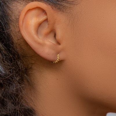 Brinco pequeno dourado em argola com textura de bolinhas na orelha direita