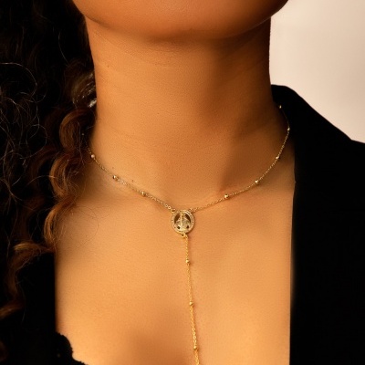 Colar dourado com pingente redondo e cruz em pescoço de mulher com roupa preta