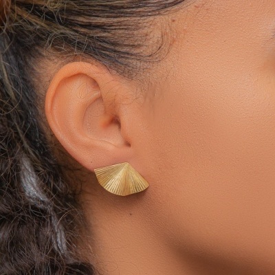Brinco dourado formato concha com textura em linhas radiantes no ouvido de mulher.