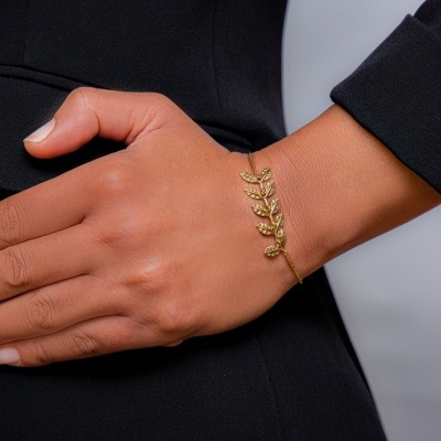 Pulseira dourada de folhas num pulso sobre roupa preta