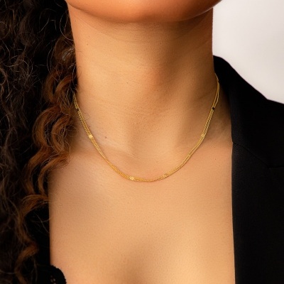 Colar dourado fino no pescoço de mulher com roupa preta