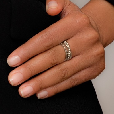 Anel prateado com textura em bolinhas na mão de uma pessoa com pele castanha, roupa preta