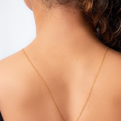 Colar dourado com pendente quadrado numa mulher de costas