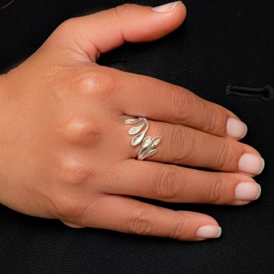 Mão com anel prateado de folhas sobre tecido preto