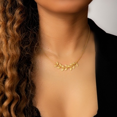 Colar dourado com pendente de folhas numa pessoa com blusa preta e cabelo castanho ondulado