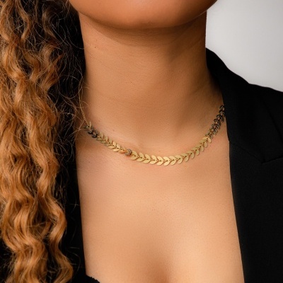 Colar de ouro com elos em forma de folhas no pescoço de mulher com roupa preta