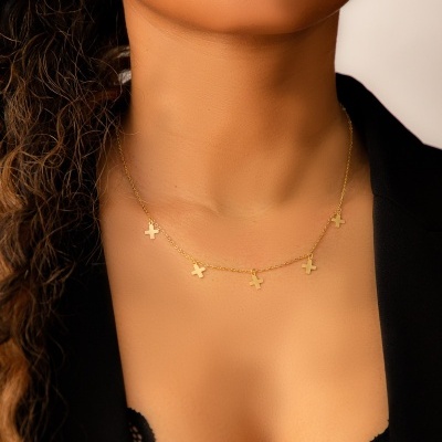 colar dourado com quatro cruzes em pescoço de mulher com blazer preto e top de renda