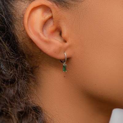 Brinco pendente prateado com pedra verde na orelha de uma pessoa