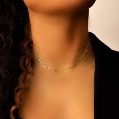 Colar dourado fino usado no pescoço de mulher com blusa preta e cabelo encaracolado