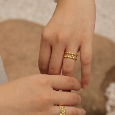 Mãos a usar anéis dourados com diferentes designs contra fundo neutro