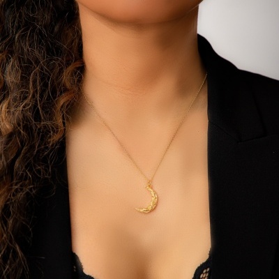 Colar dourado com pendente de lua em mulher de pele morena com roupa preta