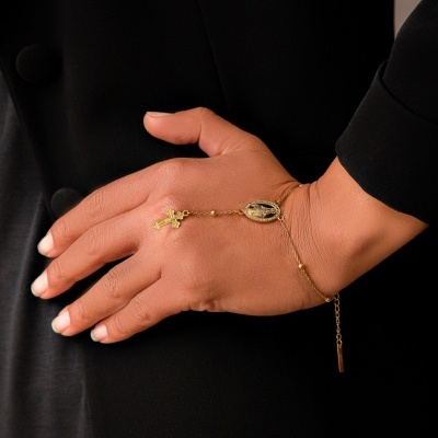 Pulseira dourada com crucifixo e medalhão oval numa mão com roupa preta