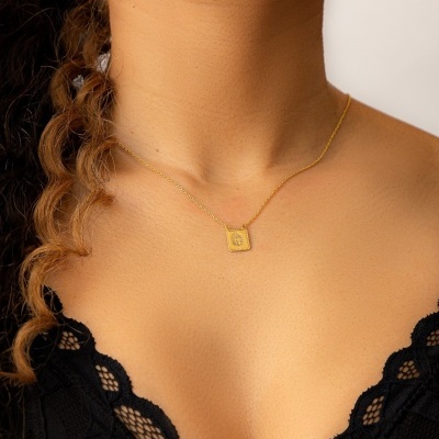 Colar dourado com pendente quadrado e top preto de renda num pescoço e peito feminino