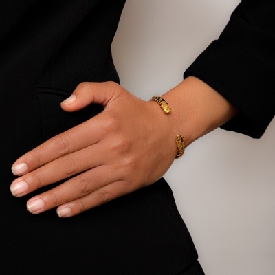 Pulseira dourada aberta em pulso sobre roupa preta