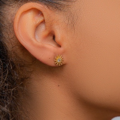 Brinco dourado em forma de estrela com detalhe brilhante no centro na orelha de uma pessoa